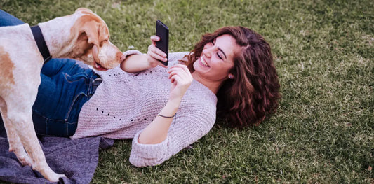 Pet owner taking a photo of her dog while lying in the grass