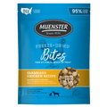 A blue Muenster dog food bag featuring a chicken silhouette, text about freeze-dried bites, and a circular window showing small, brown food pieces.